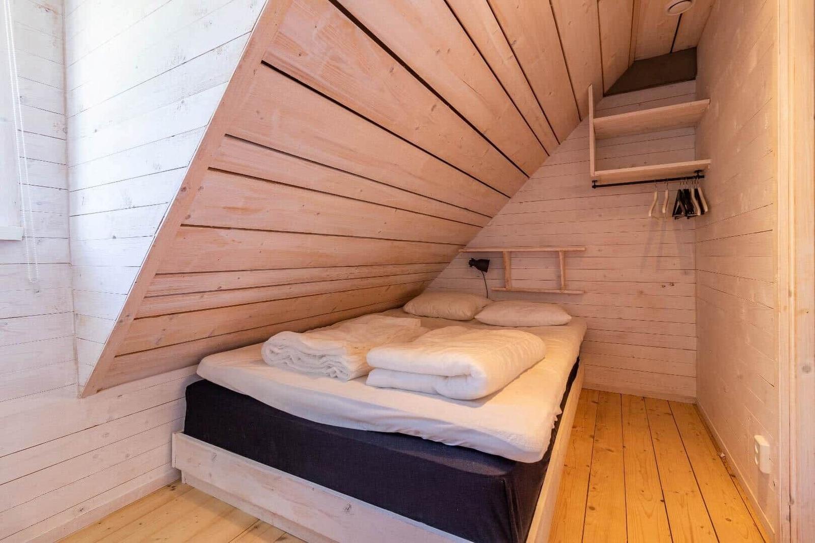 Schlafzimmer mit Dachschrägen, Bett, Kleiderständer und Holzwand.