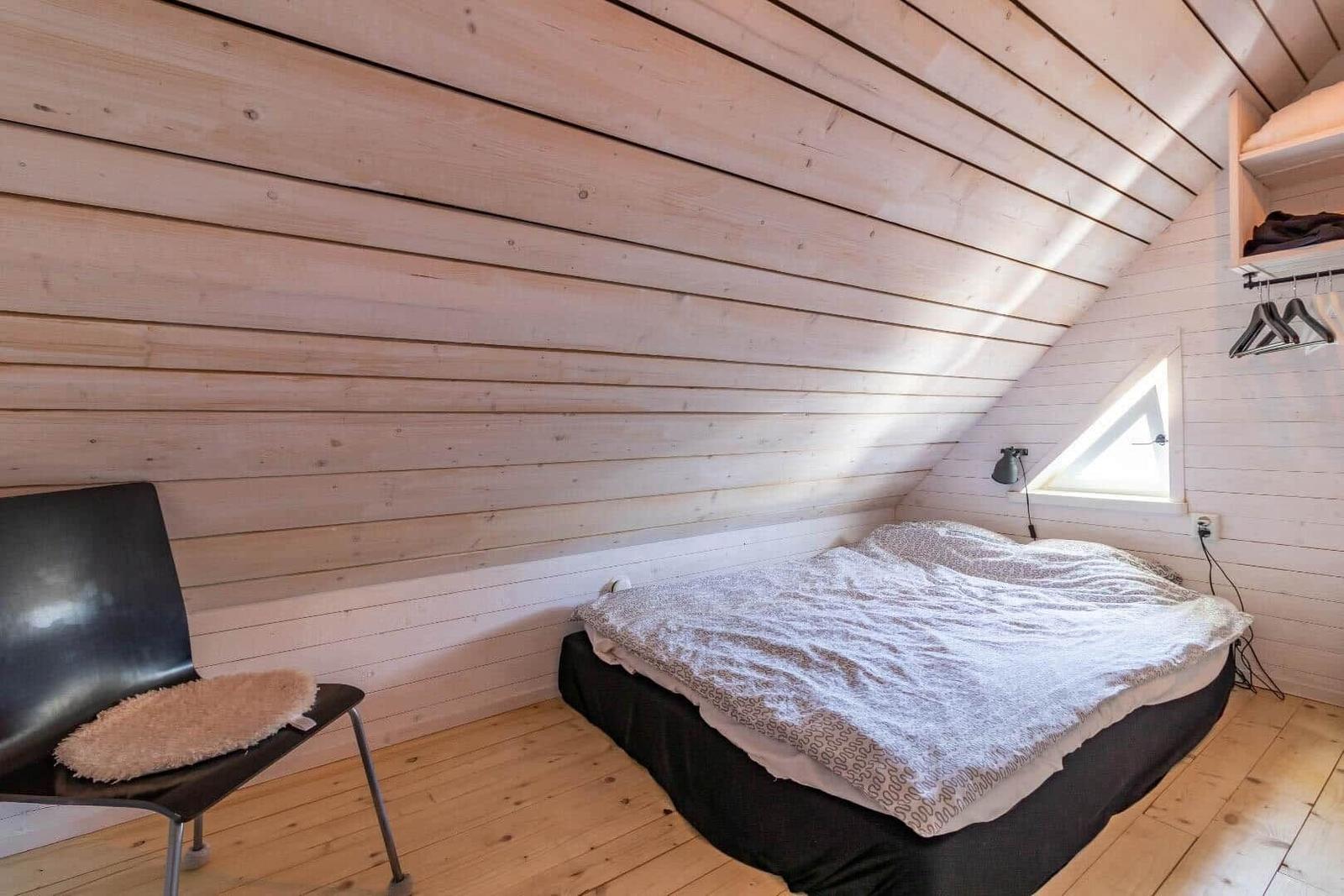 Schlafzimmer mit Dachschrägen, Bett, Stuhl und Kleiderhaken.