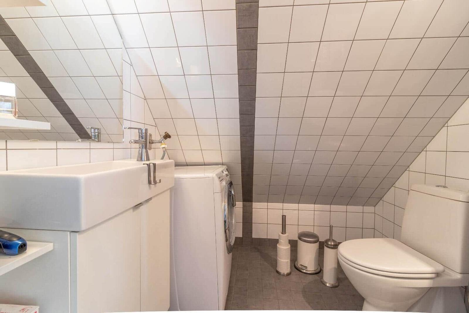 Badezimmer mit Waschmaschine, Toilette und Spiegel an schrägen Wänden.