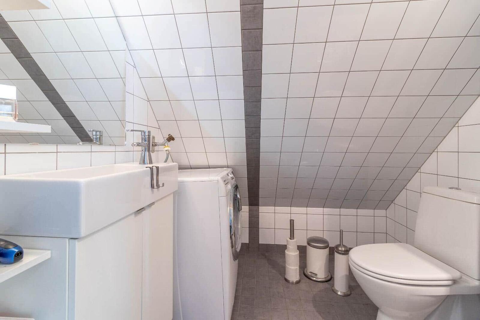 Badezimmer mit Waschmaschine, Toilette und Spiegel an geneigter Wand.