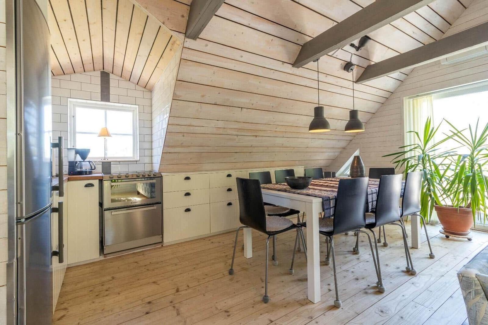 Küche mit Essbereich unter Holzdach, Küchenschränke, Tisch mit Stühlen und Pflanze.