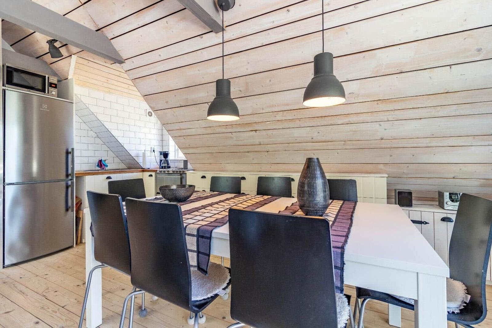 Essbereich mit Tisch, Stühlen und Küchenzeile unter Holzdecke.