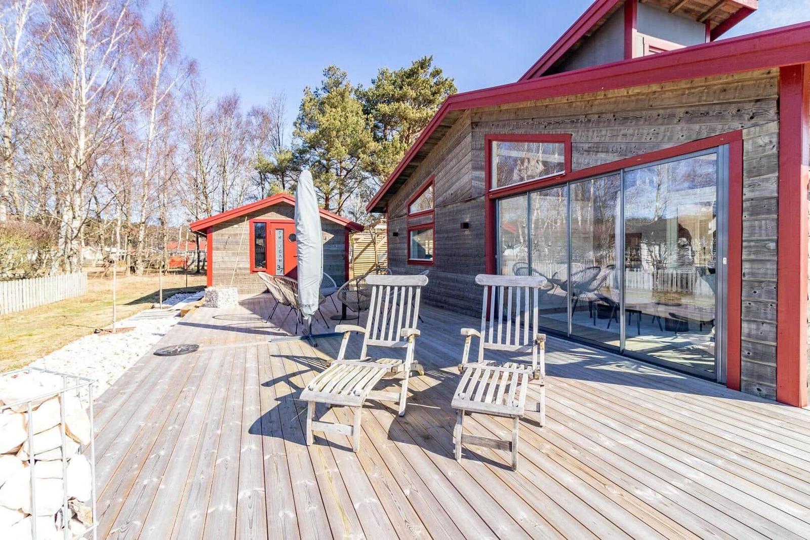 Holzterrasse mit zwei Liegestühlen und Glasfront zum Haus.