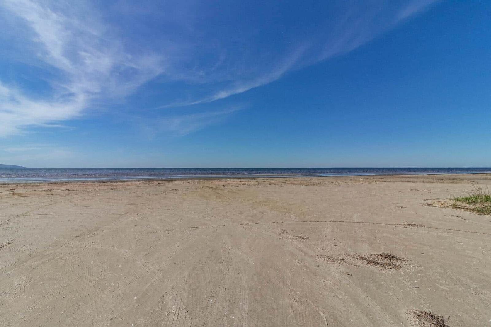 Weiterer Sandstrand mit klarem Himmel und ruhigem Meer.