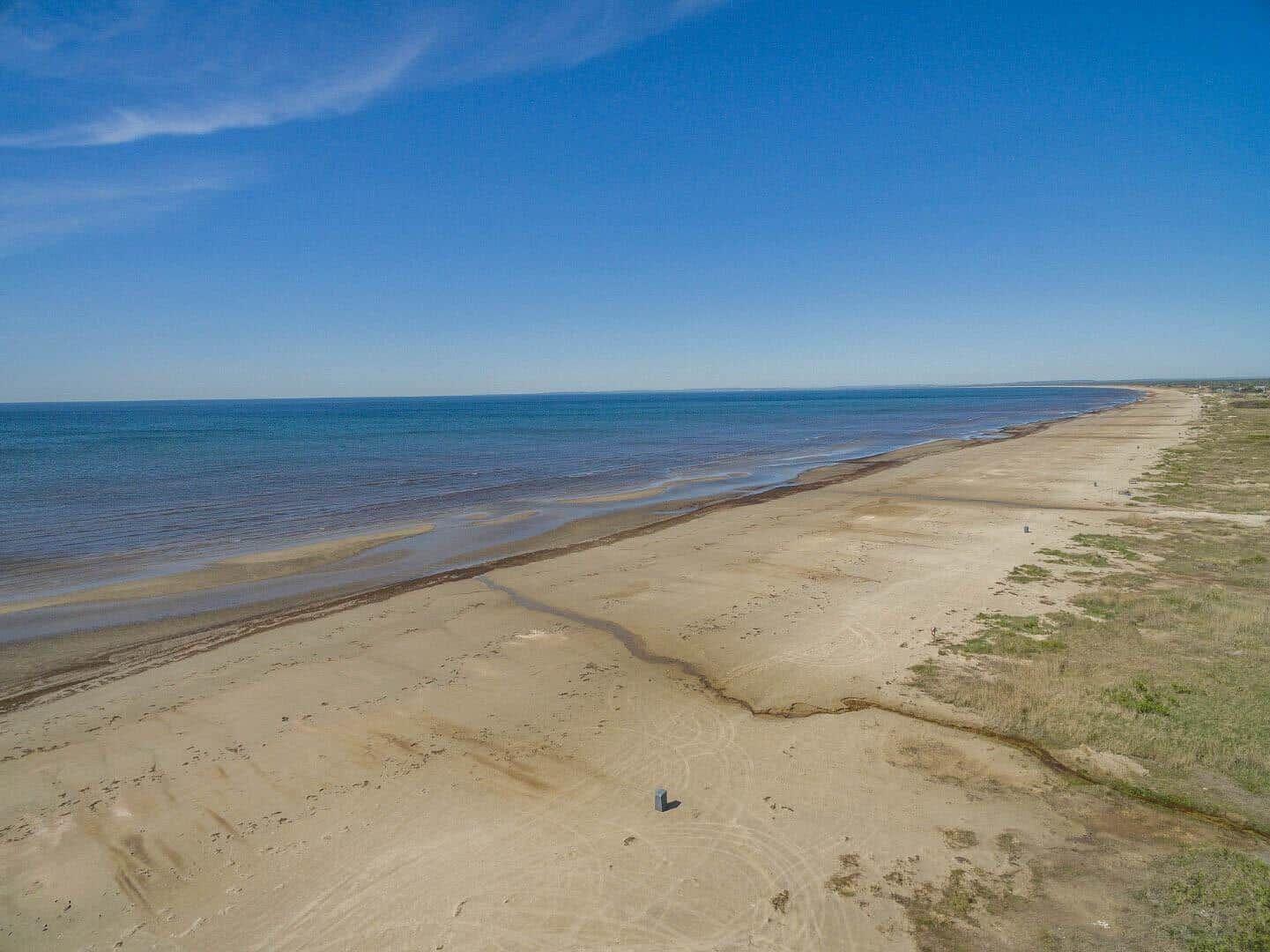 Weiterer Strandabschnitt mit sandigem Ufer und ruhigem Meer unter blauem Himmel.