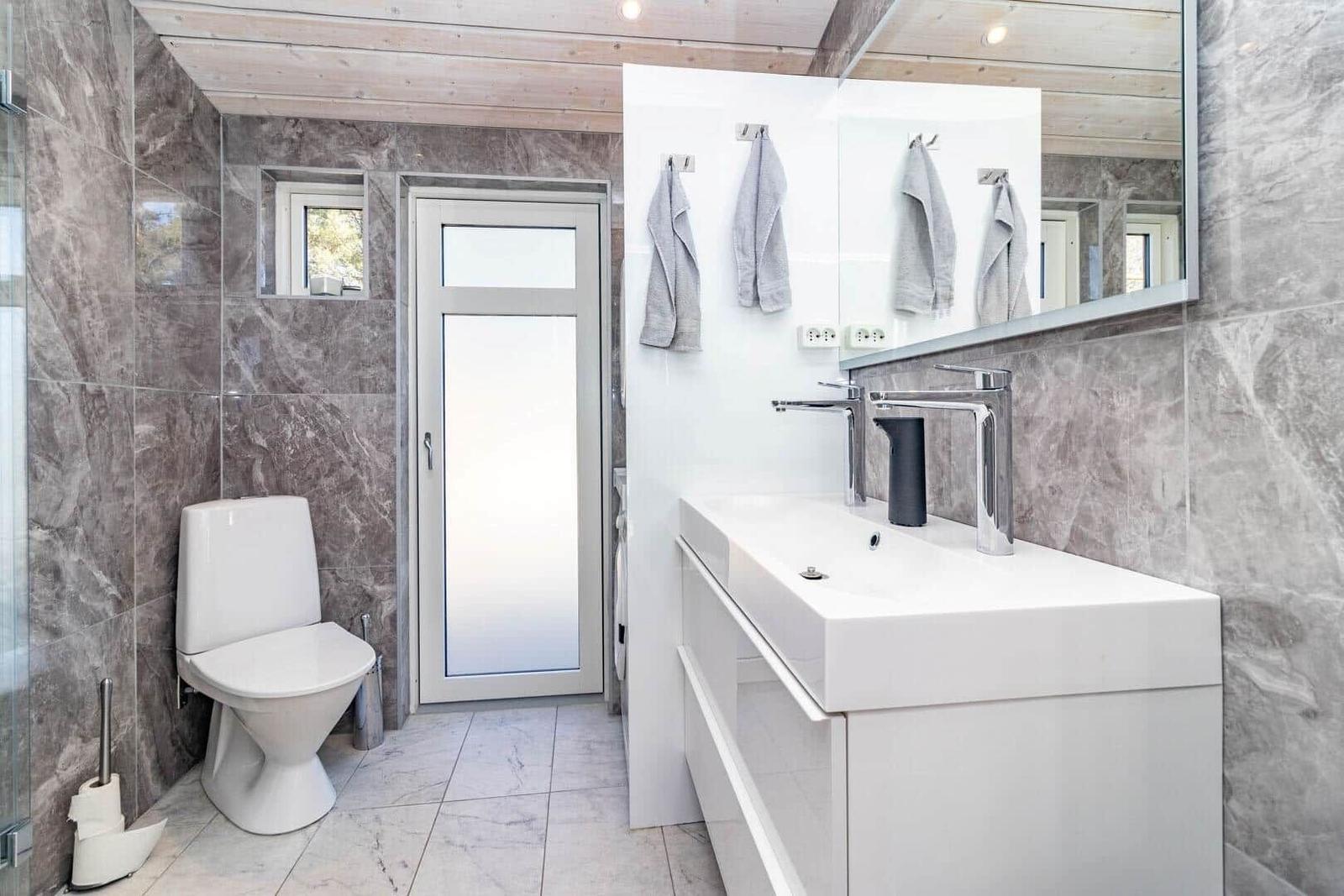 Badezimmer mit Toilette, Waschbecken und Dusche. Marmortönen und Holzdecke.