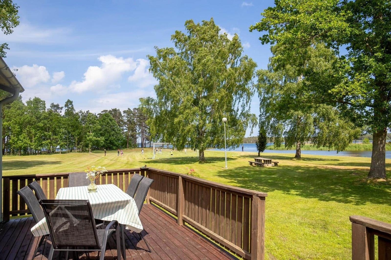 Terrasse mit Tisch und Stühlen blickt auf grünen Rasen und See.