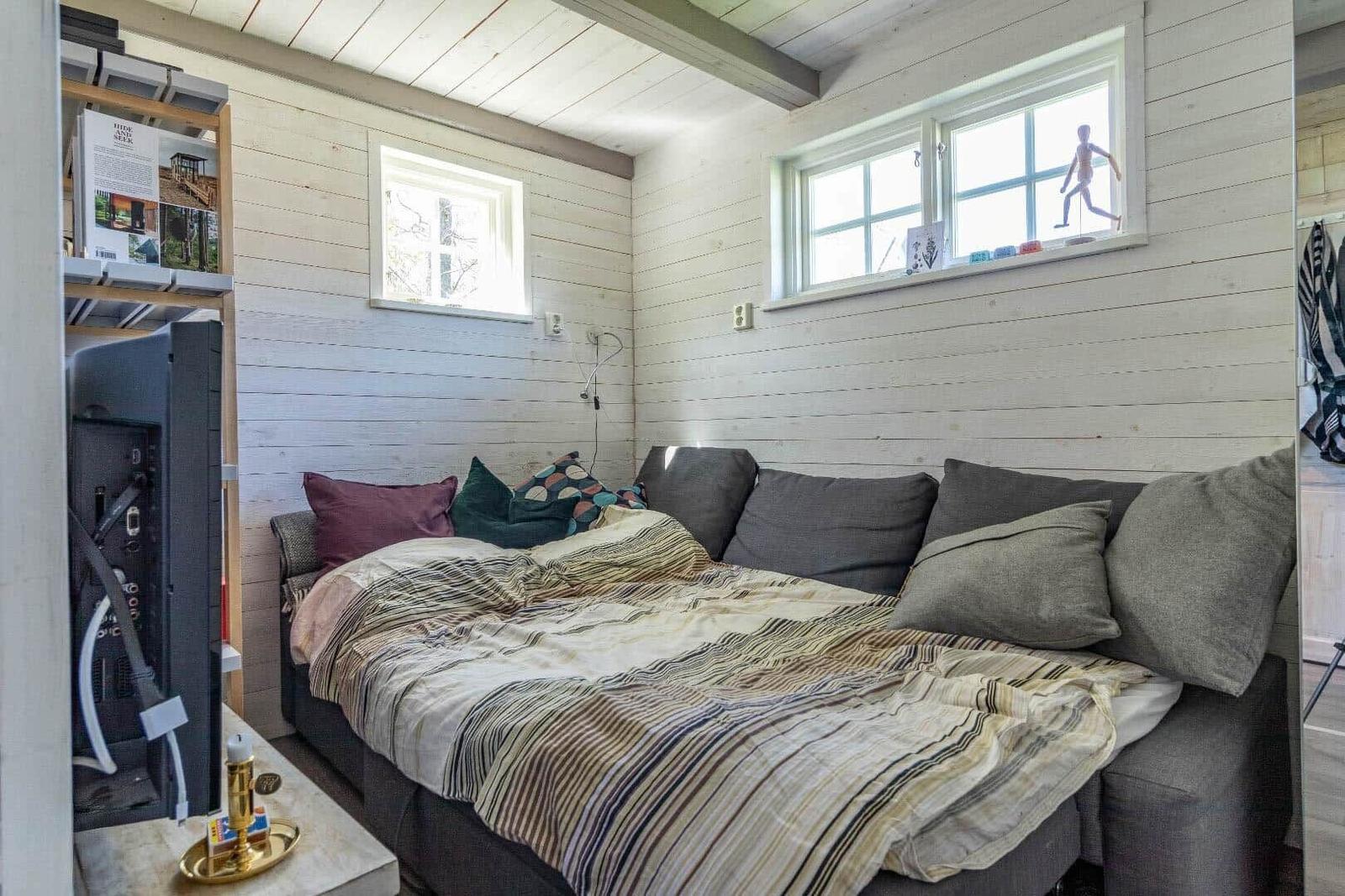 Schlafzimmer mit Sofa-Bett, Fenstern und Holzwänden.