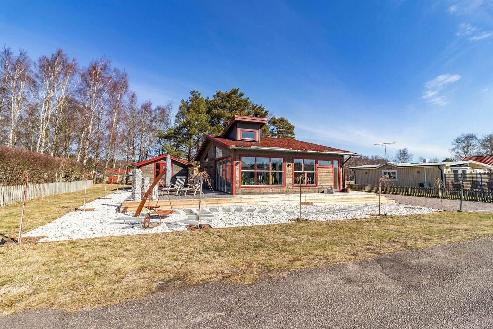 Ein Haus mit rotem Dach und Holzfassade. Vorgarten mit Steinen und Sitzgelegenheit.