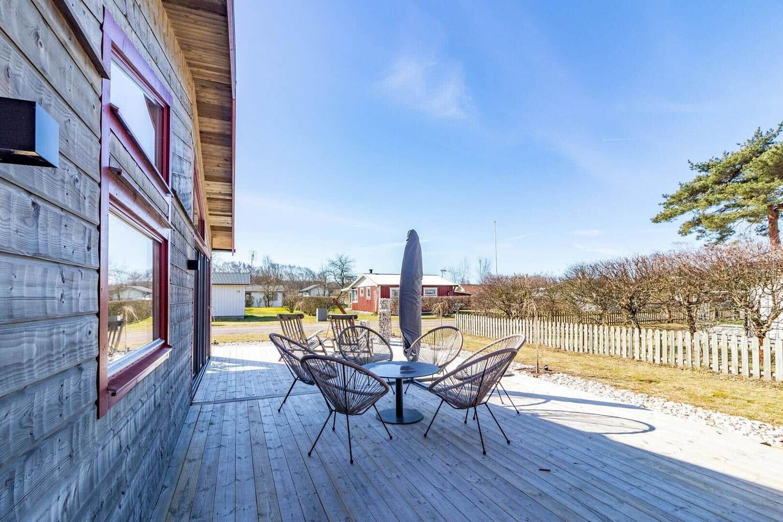 Terrasse mit Tisch und Stühlen neben Holzhaus mit roten Fensterrahmen.