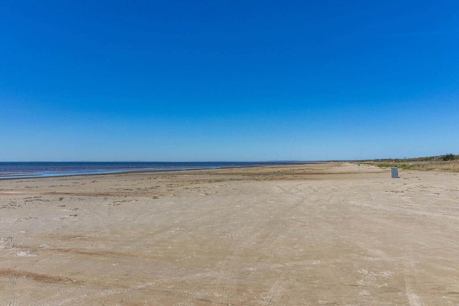 Weiterer Sandstrand mit klarem Himmel und ruhigem Meer im Hintergrund.