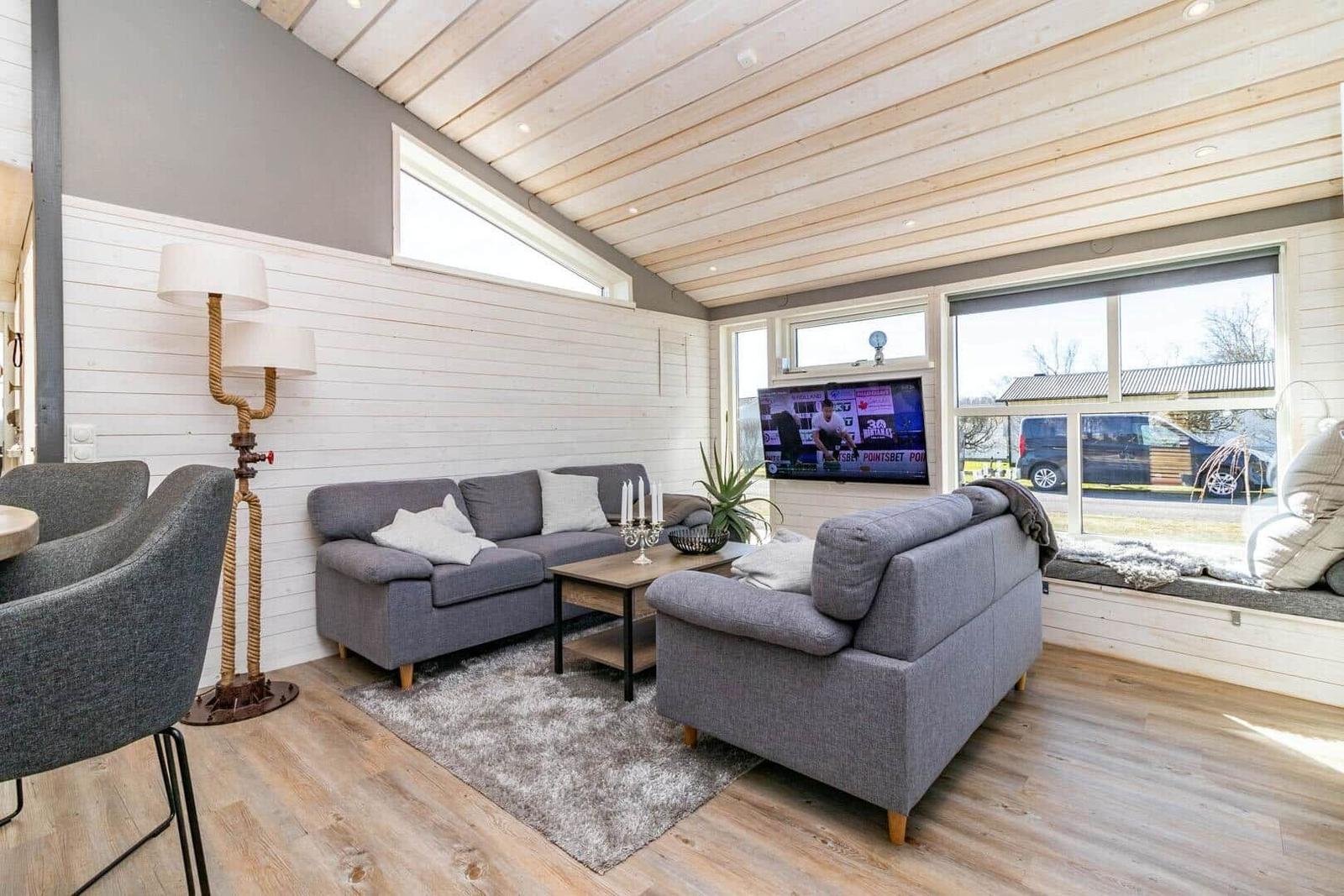 Wohnzimmer mit Sofa, Couch und Fernseher. Holzdecke und große Fenster.