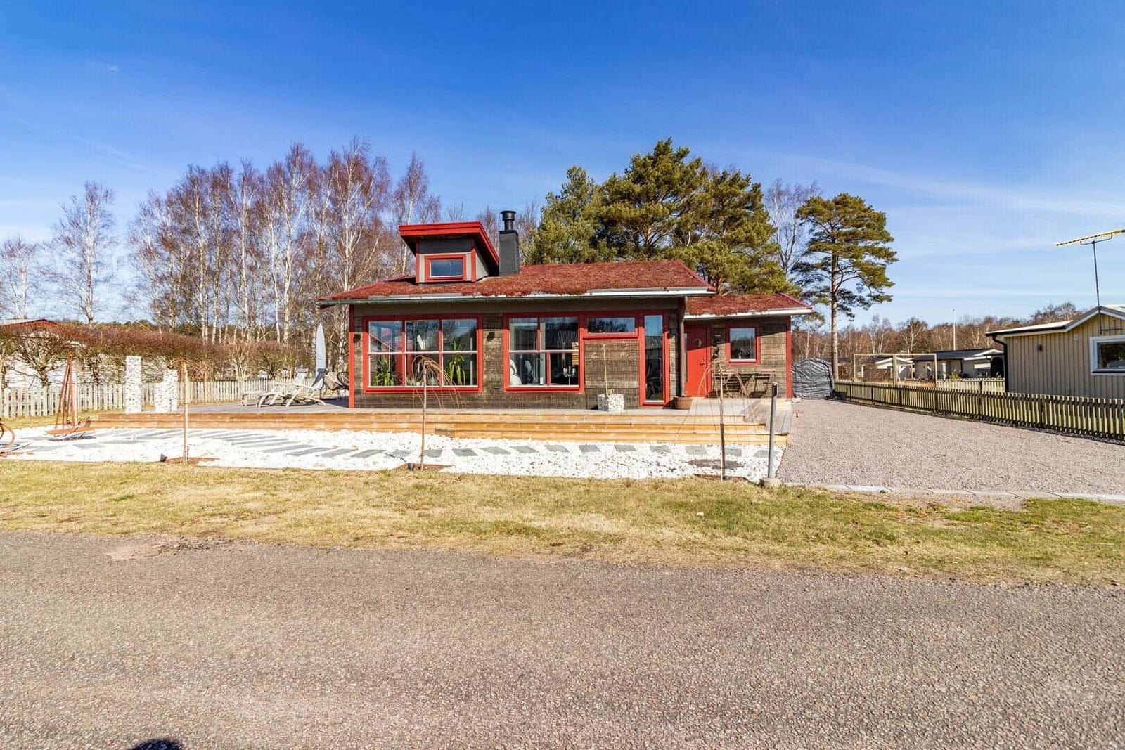 Rotes Holzhaus mit Terrasse und Garten. Umgeben von Bäumen und klarer Luft.