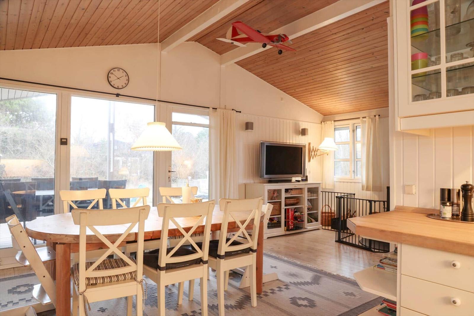 Essbereich mit Holztisch, Stühlen und Fernseher. Holzdecke und große Fenster.