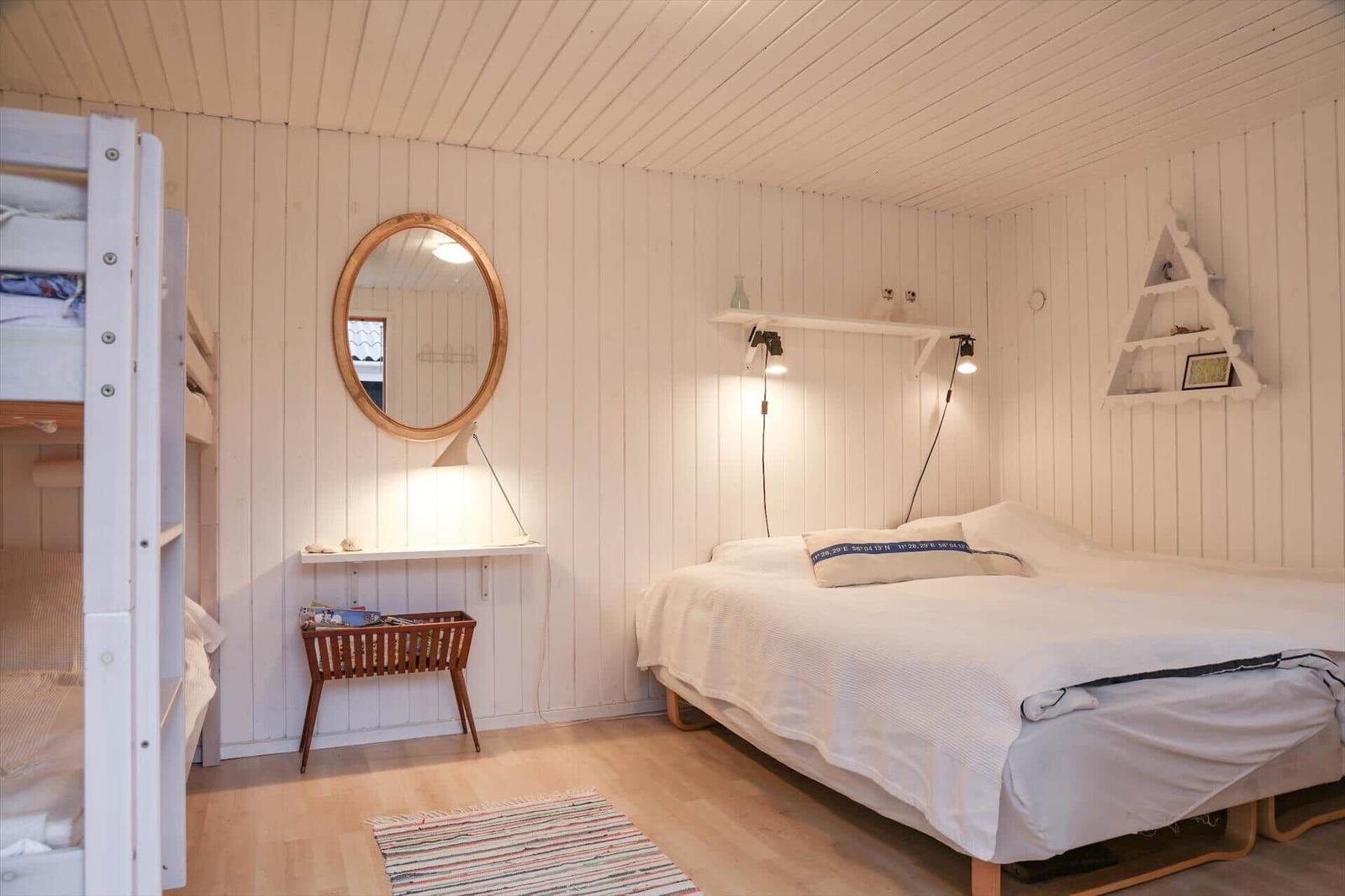 Schlafzimmer mit Doppelbett, Krippe, Spiegel und Wandregal.