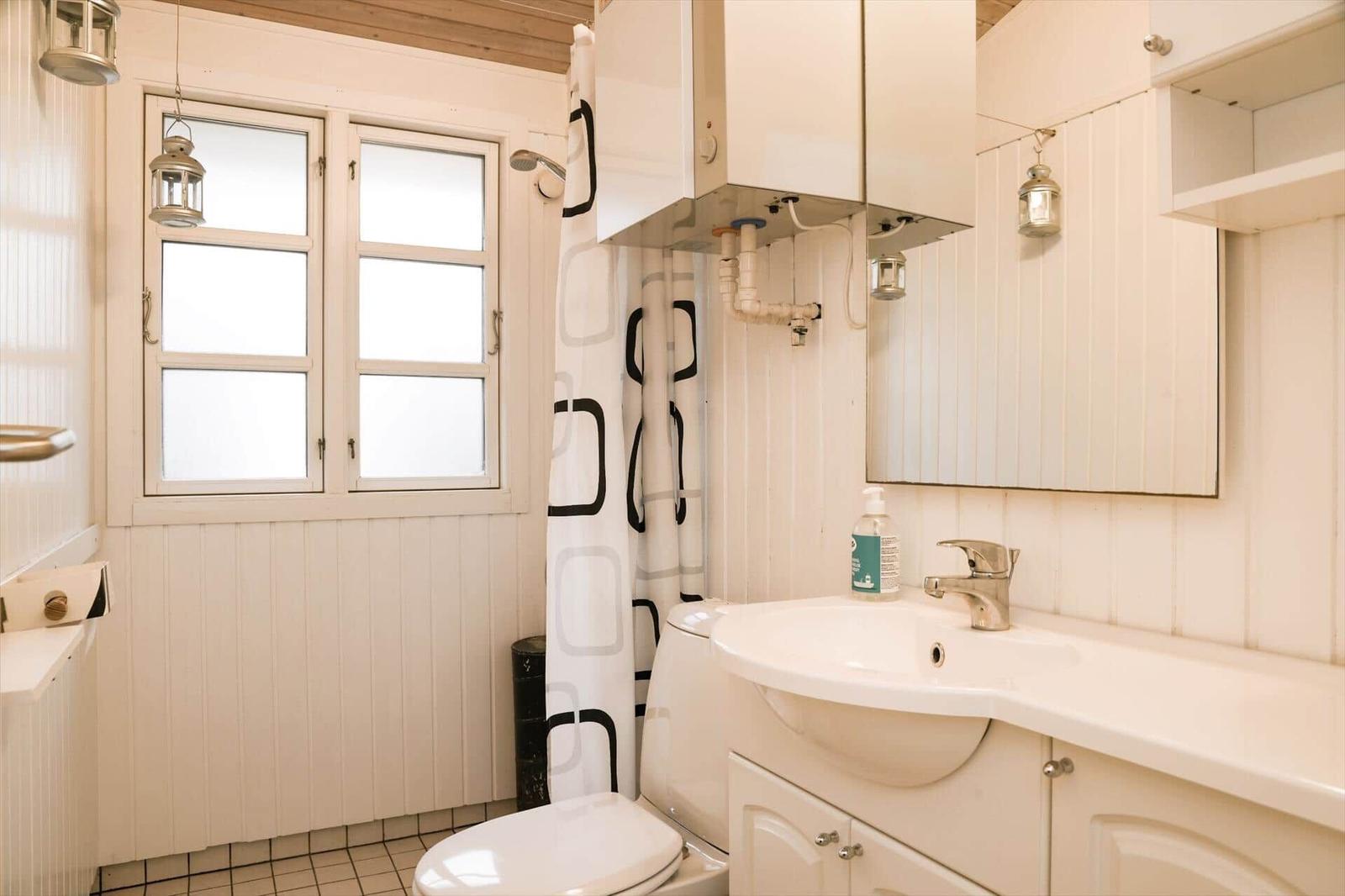 Badezimmer mit Toilette, Waschbecken und Dusche. Weiße Holzwände und Fenster.