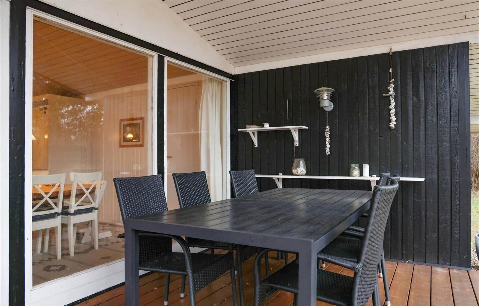 Terrasse mit Tisch und Stühlen, schwarze Wand und Glasfront zum Innenraum.