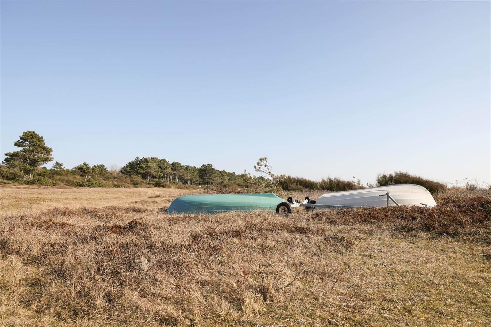 Zwei Boote auf einem Anhänger liegen in einem trockenen Grasfeld.
