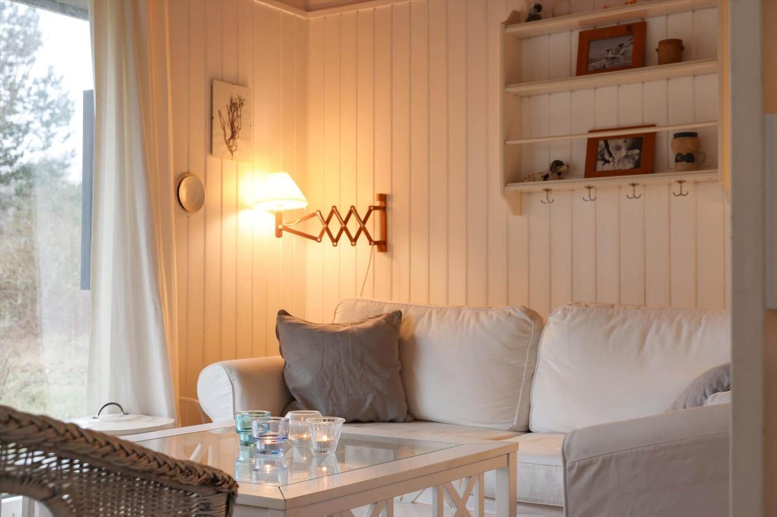 Wohnzimmer mit Sofa, Glas-Tisch und Wandregal. Fensterblick auf Wald.