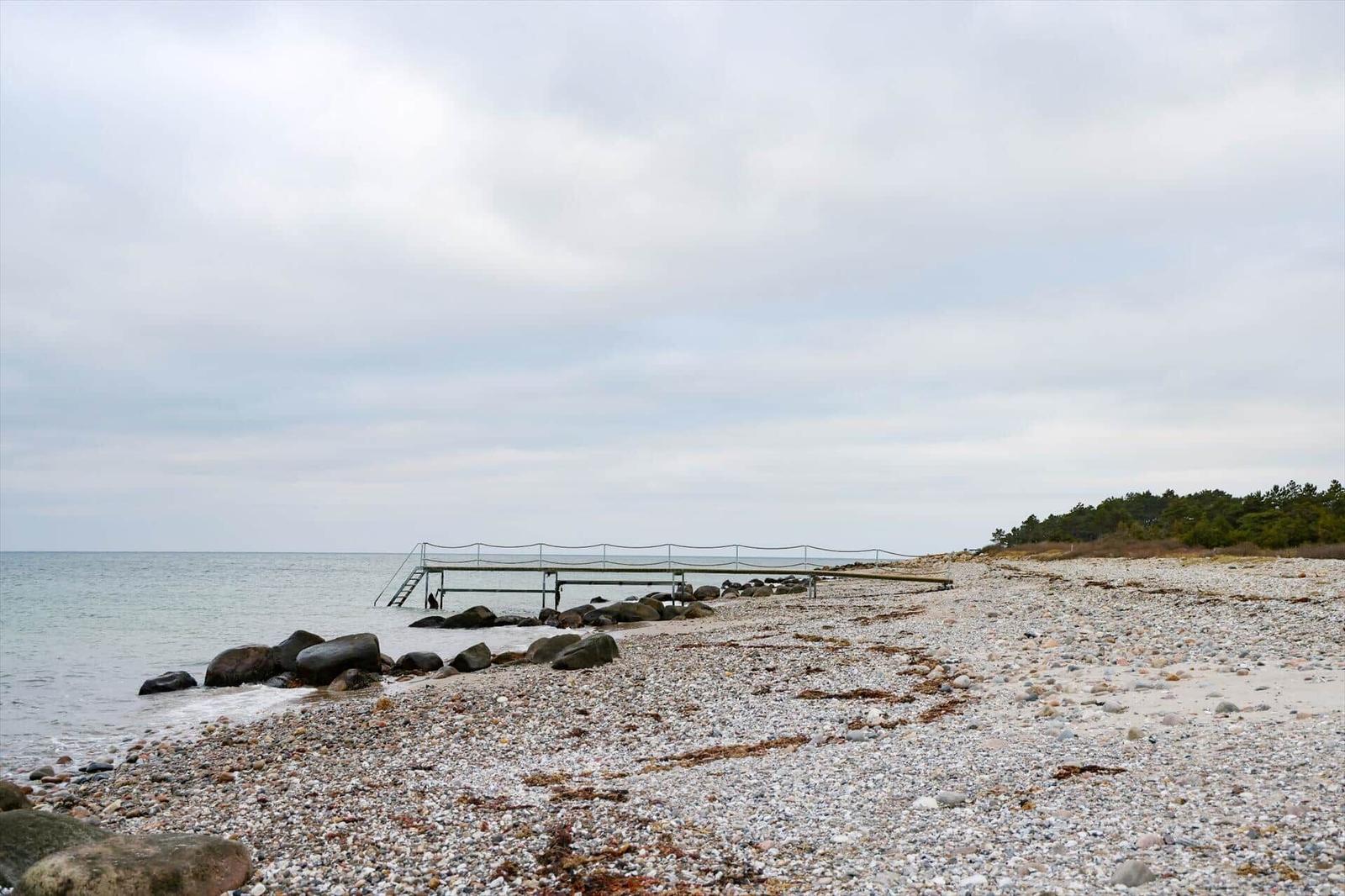 Steiniger Strand mit Bootssteg und Blick aufs Meer.