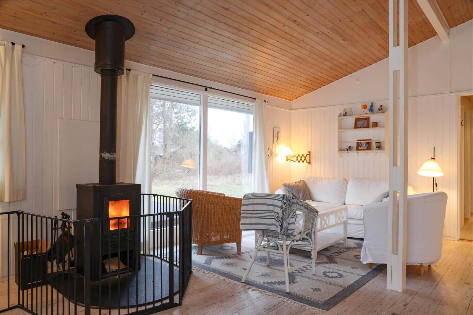 Wohnzimmer mit Kamin, Sofa, Sessel und großem Fenster. Holzdecke und -boden.