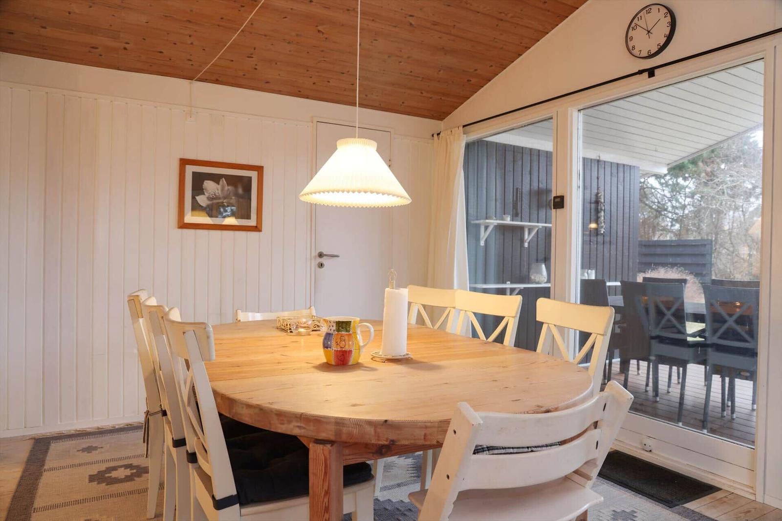 Essbereich mit runden Tisch und Stühlen, Glasfront zum Balkon, Holzdecke und Wand.