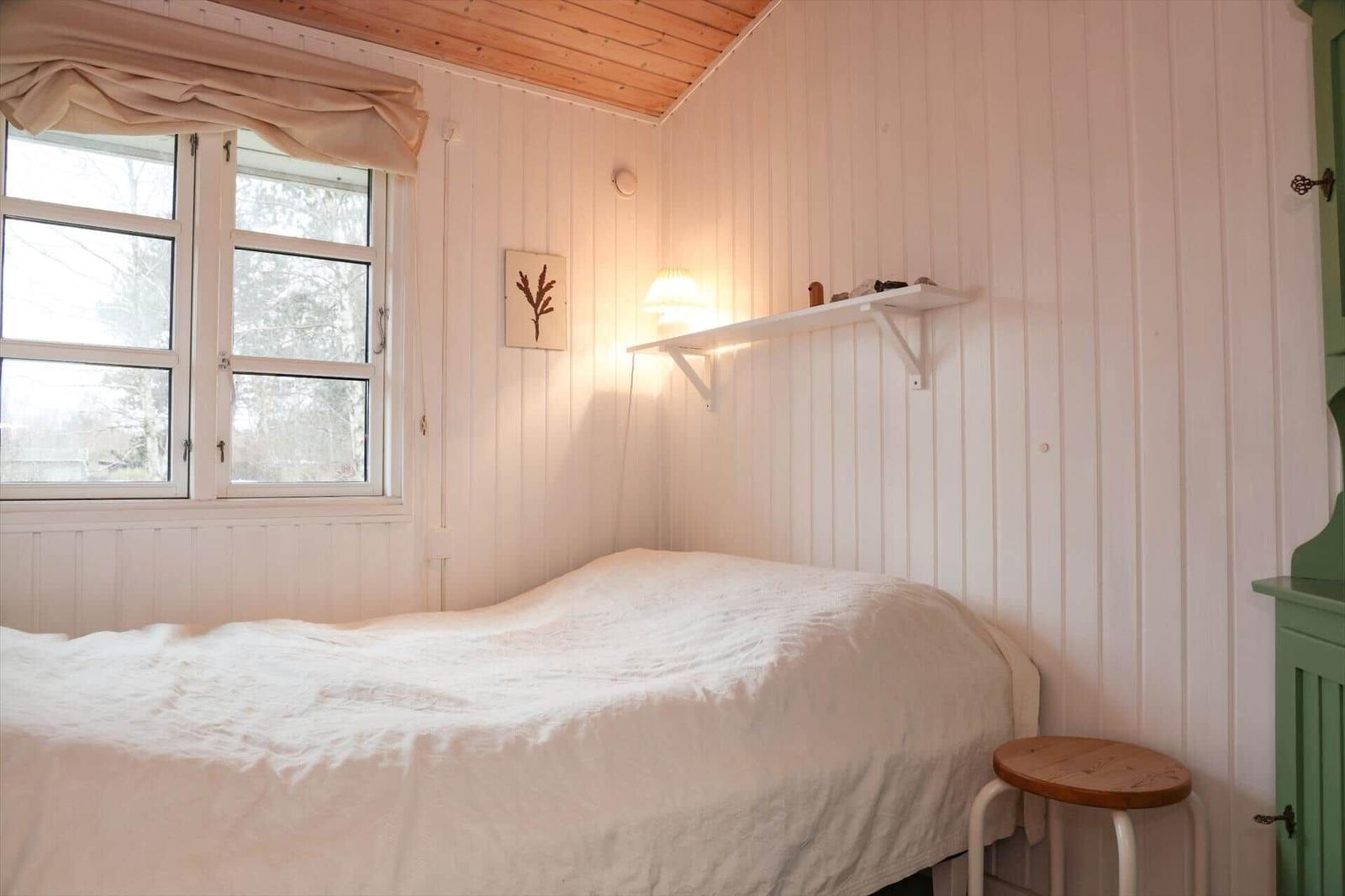 Ein Schlafzimmer mit Bett, Fenster und Wandregal.
