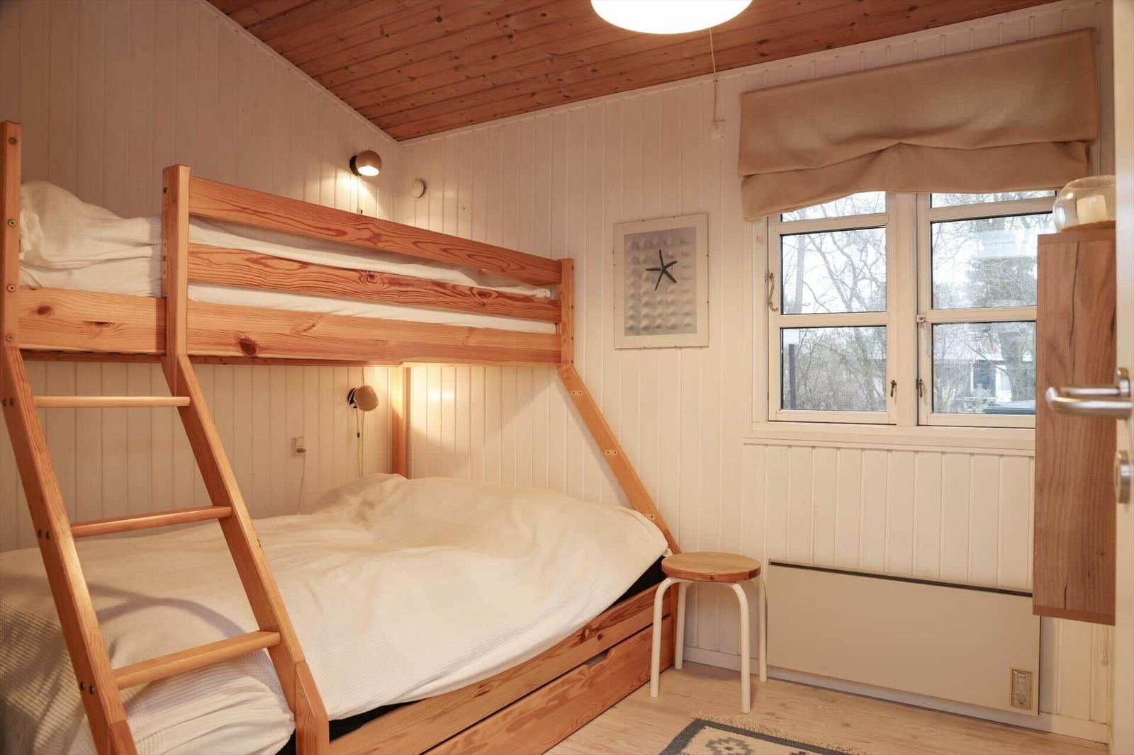 Zimmer mit Doppelstockbett, Fenster und Holzwandverkleidung.