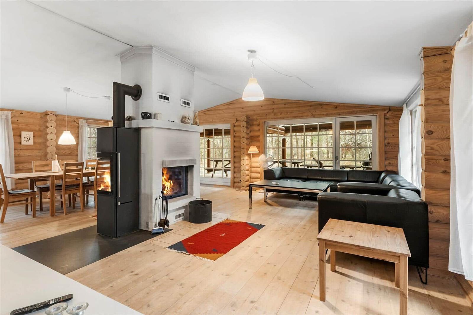 Wohn- und Essbereich mit Kamin, Holzwand und schwarzen Sofas.