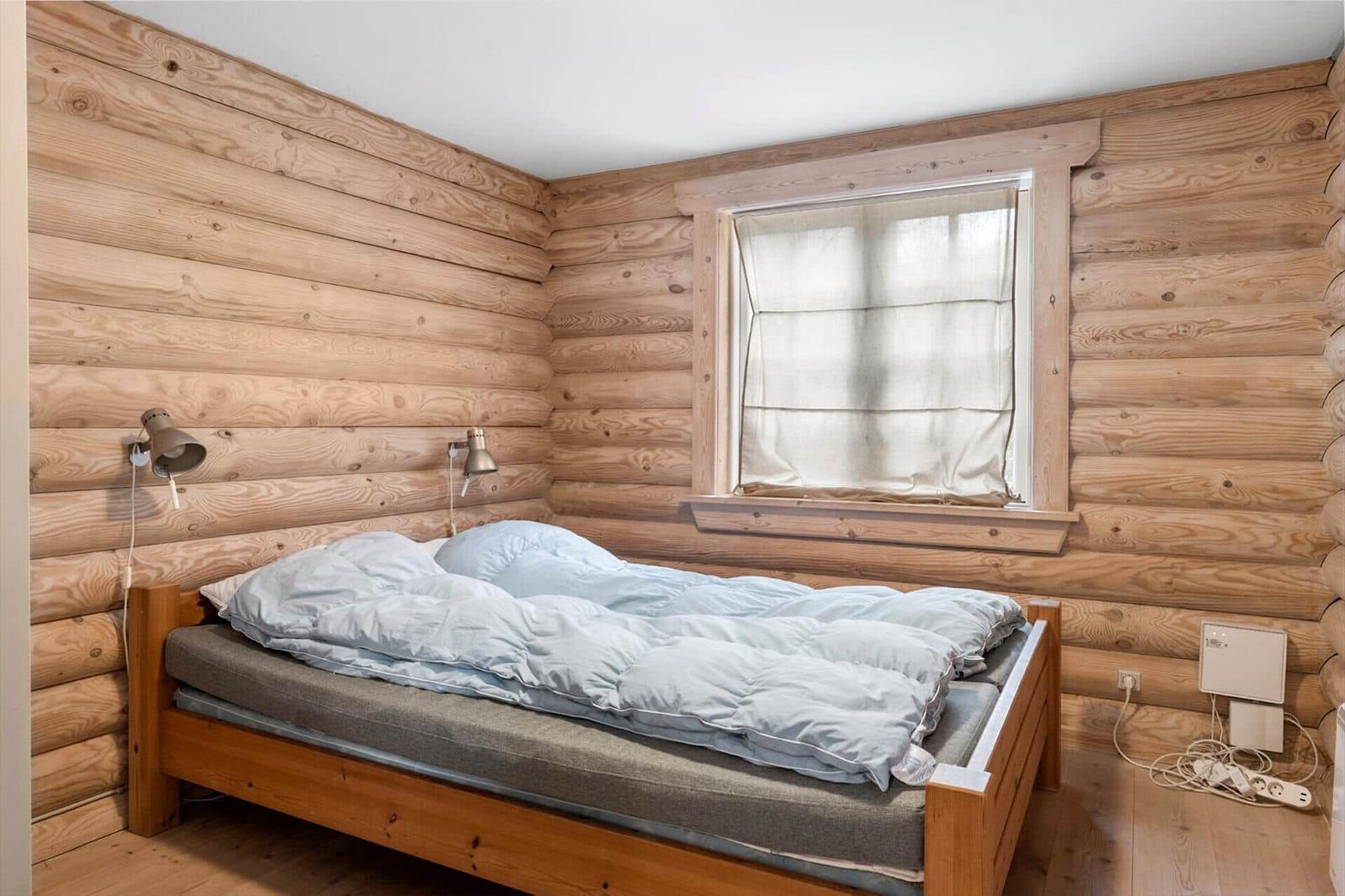 Schlafzimmer mit Holzwand, Bett und Fenster mit Vorhang.