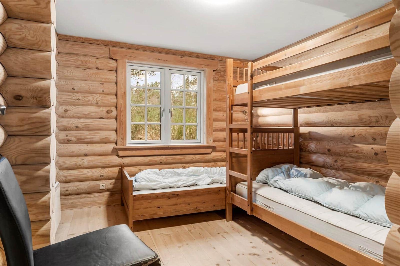 Zimmer mit Holzwand, Doppelstockbett und Fenster mit Blick nach draußen.