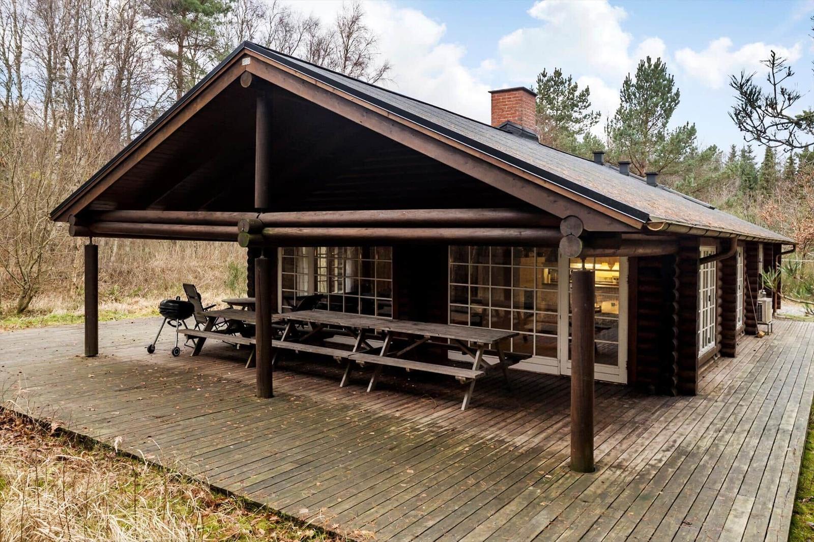 Holzhaus mit überdachtem Balkon, Picknicktisch und Grill. Umgeben von Wald.