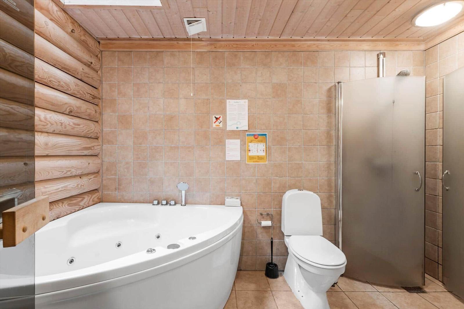 Badezimmer mit Whirlpool, Toilette und Dusche. Holzwand und Fliesen.