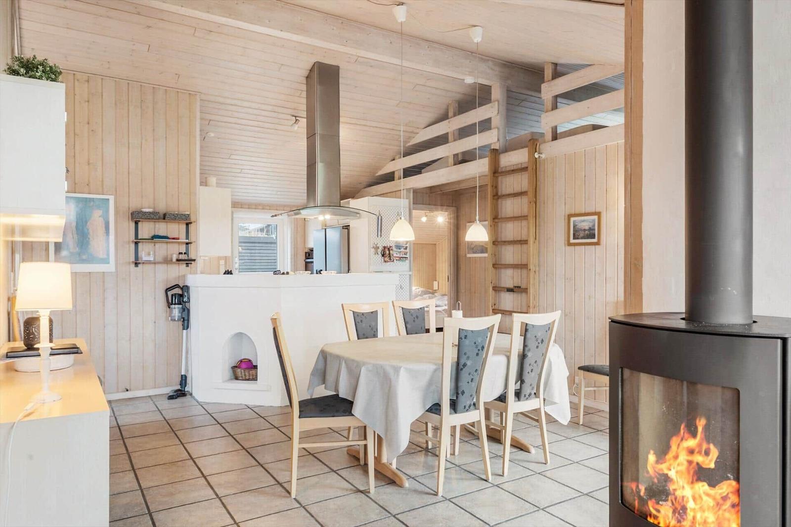 Dining area with table and chairs, wood-burning stove, and kitchen with wooden walls.