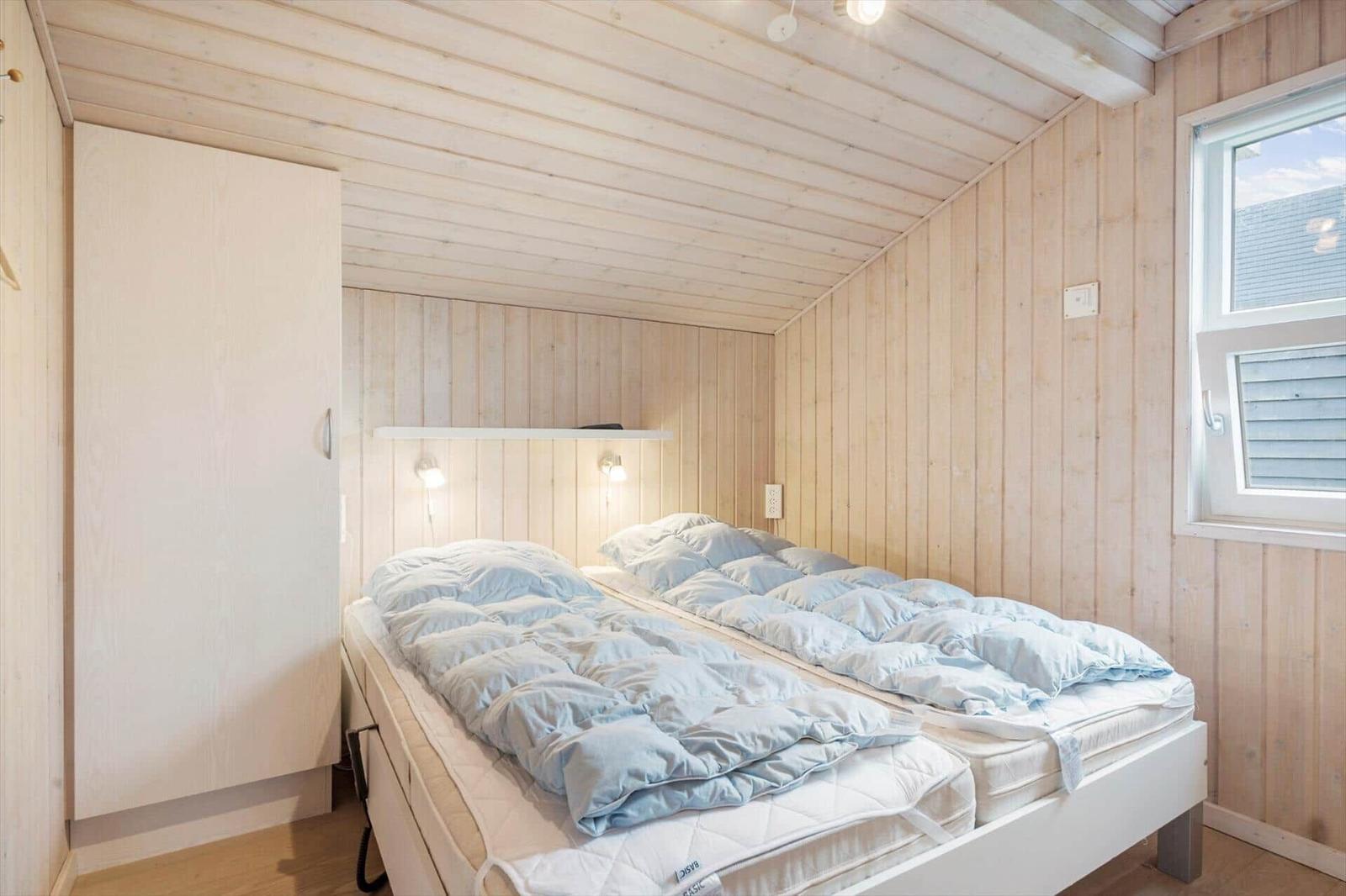 Bedroom with double bed, wood walls, and window.