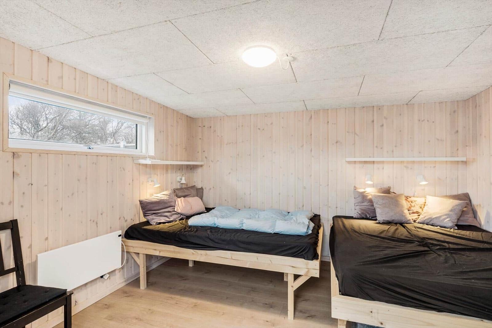 Two beds with wooden frames and bedding in a room with wooden walls and window.