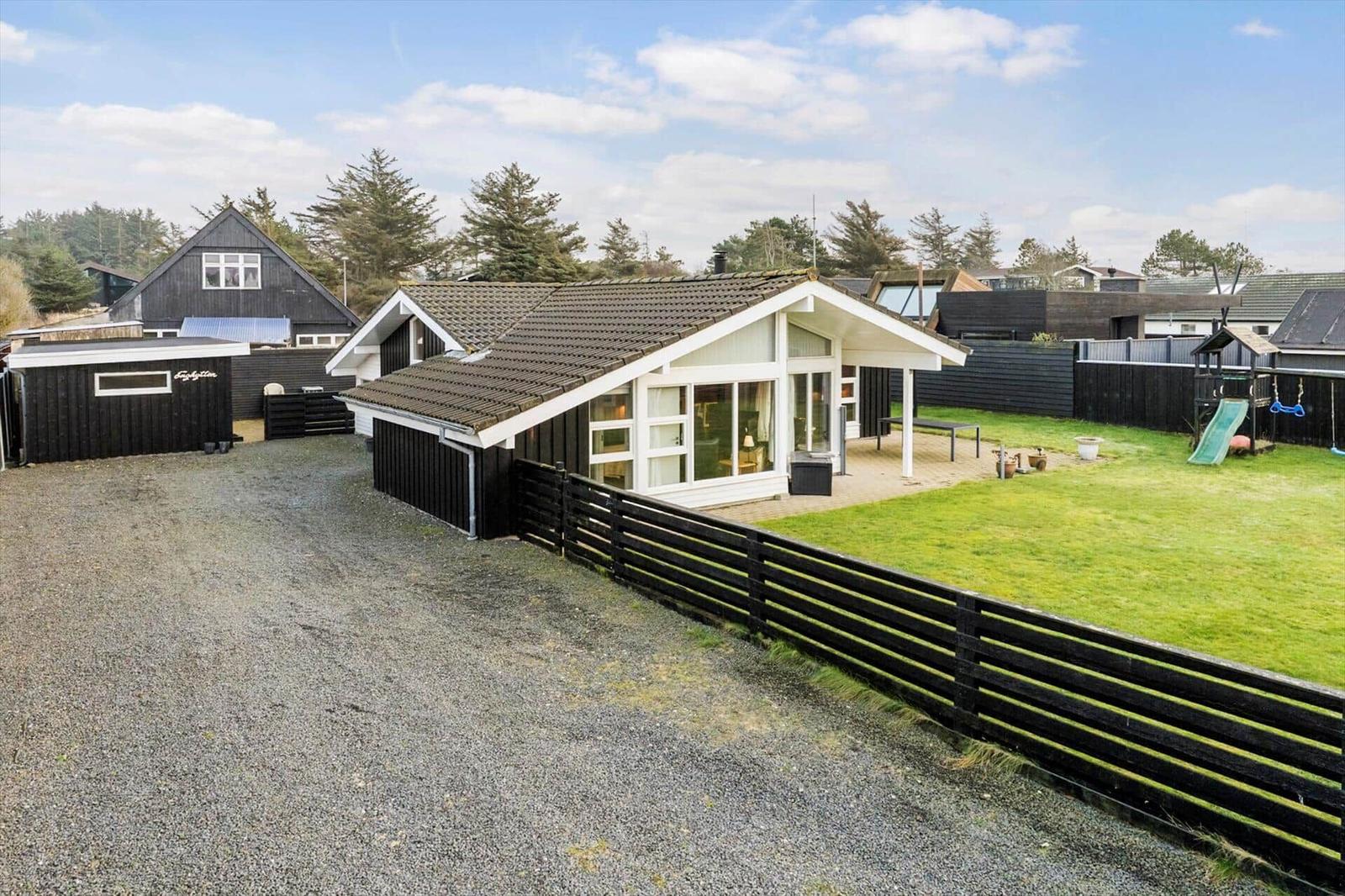 Modern villa with large garden and playground. Black timber structure and glass facade.
