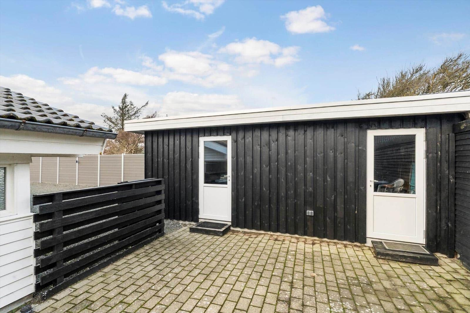 Black wooden shed with two white doors and paved outdoor area.