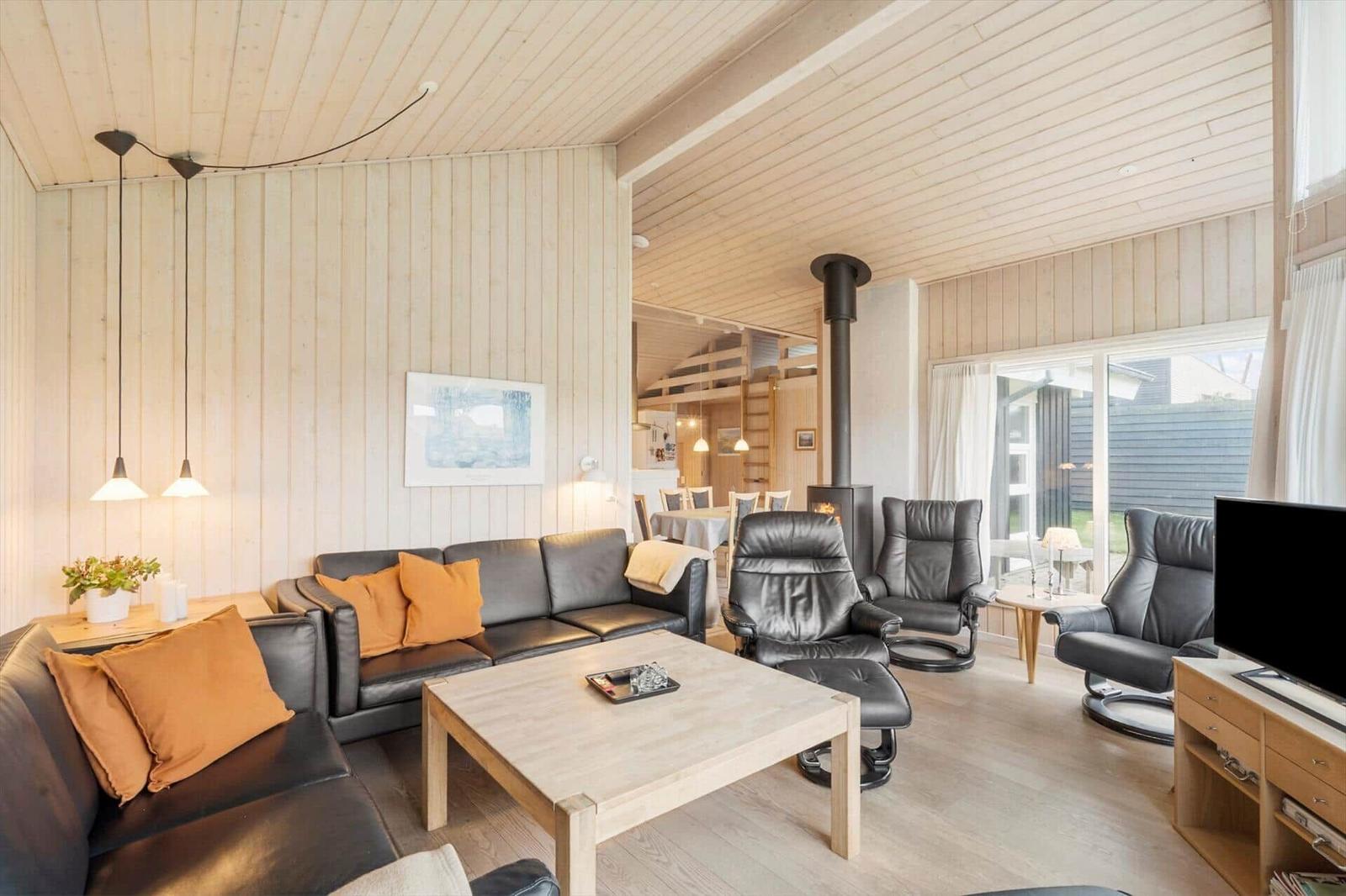 Living room with sofa, chairs, and fireplace. Wooden walls and ceiling.