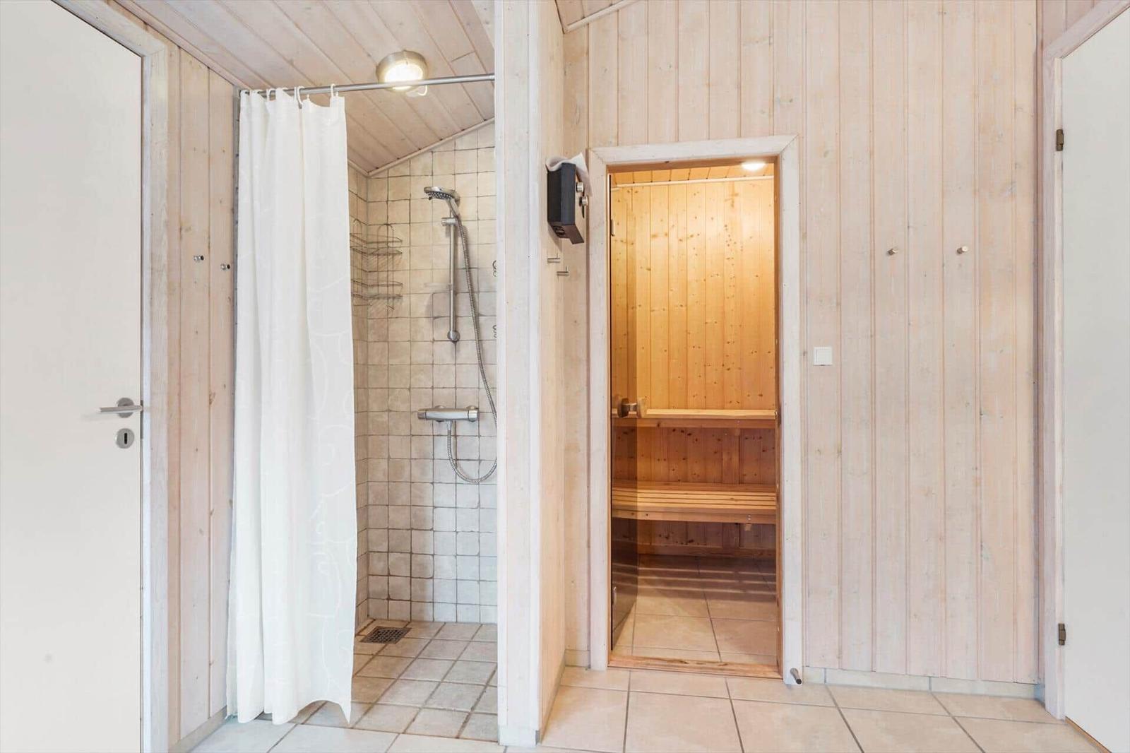 Shower with curtain and sauna in wooden house.