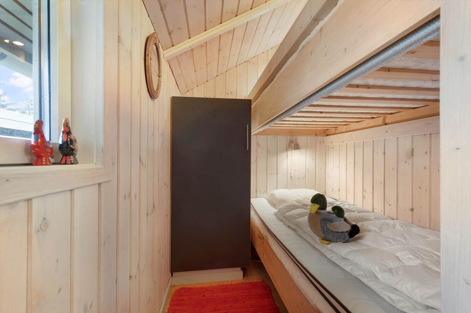 A bedroom with wooden walls, a bed, and a window. Two duck figures sit on the bed.