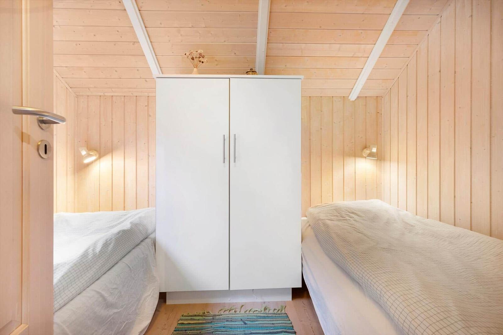 Two beds flank a white wardrobe in a wooden room.