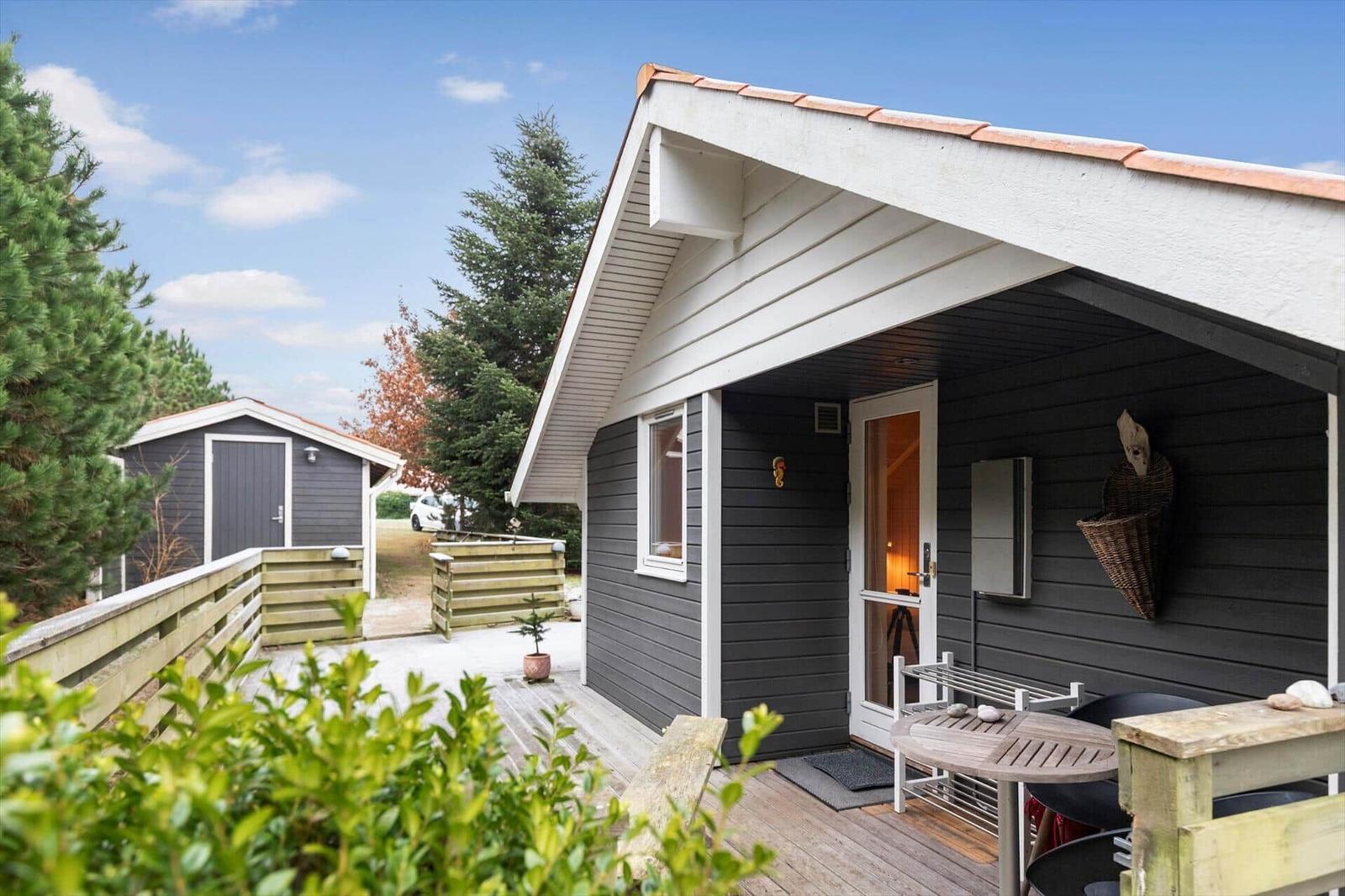 House with terrace, table and chairs. Backyard with another house and trees.