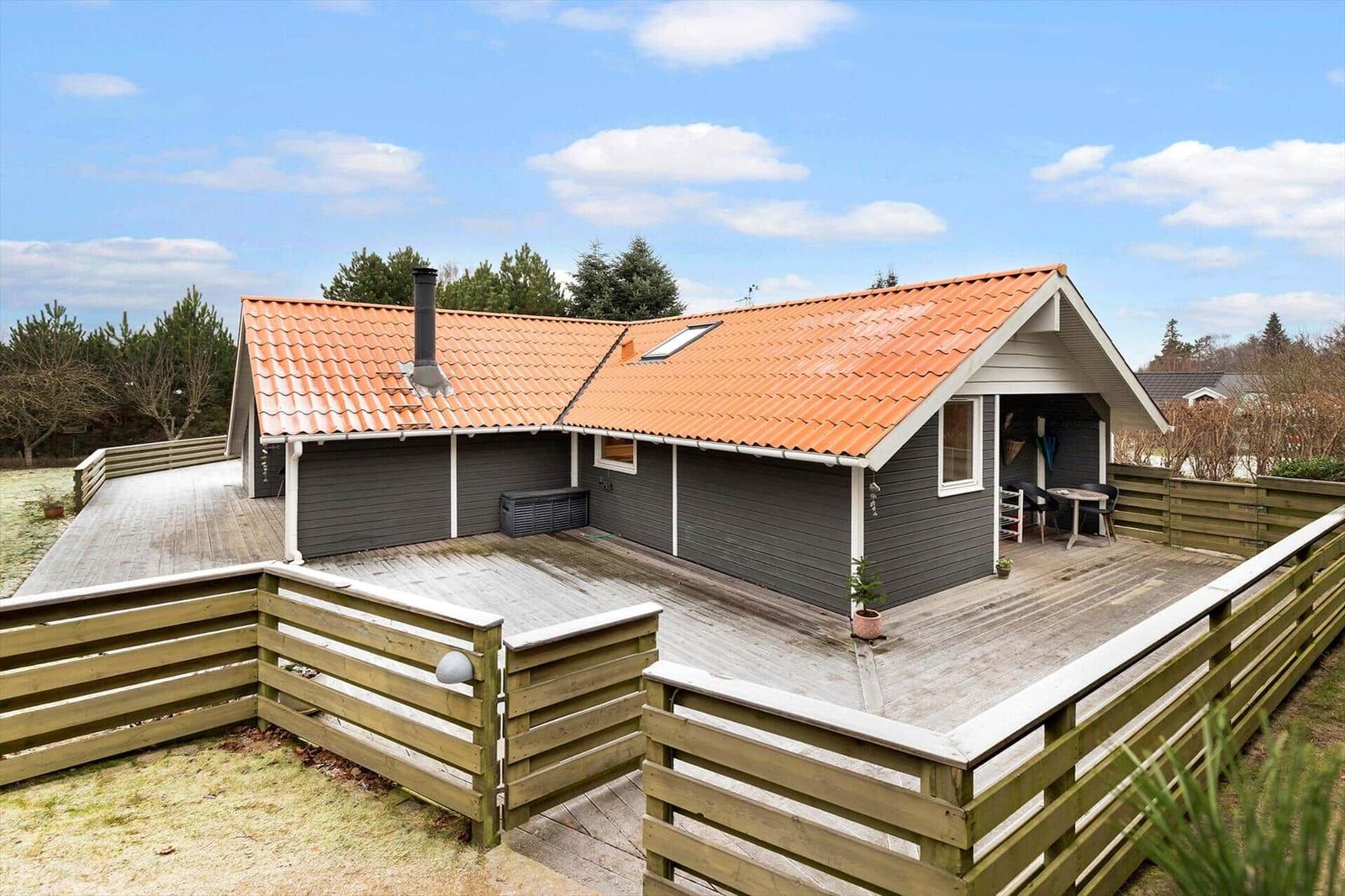 House with orange roof and wooden terrace, surrounded by a wooden fence.