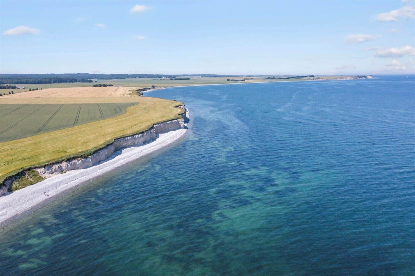 View of coastal landscape with cliff, beach, and fields