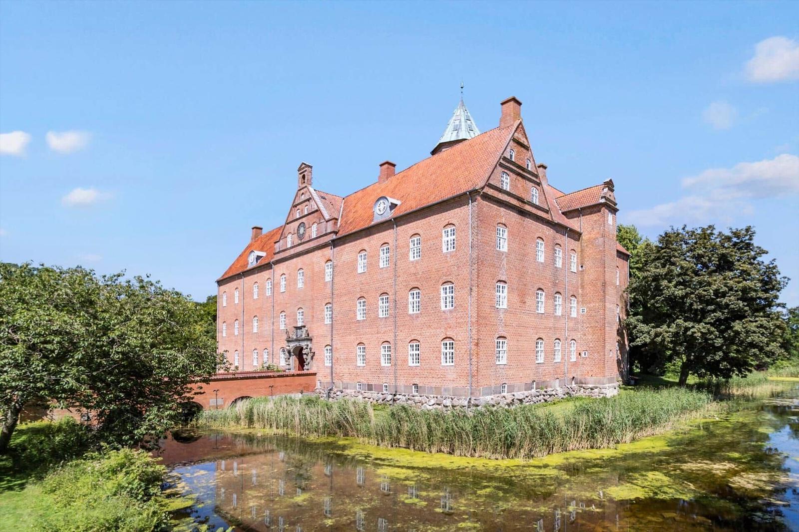 Red brick building with red roof and white windows by the water.