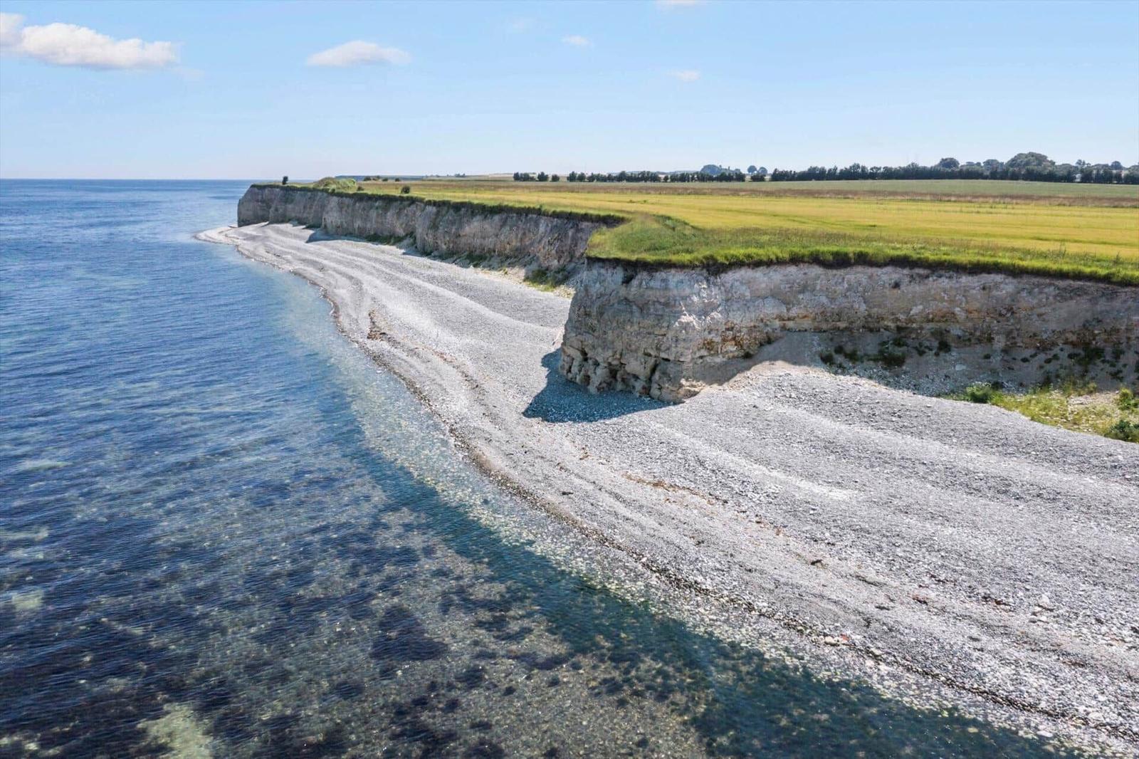 Steep cliff with beach and green fields on the horizon.