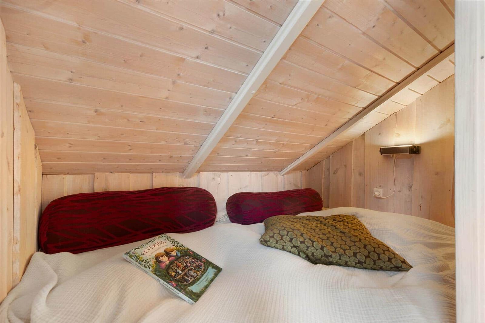 Bedroom with wooden walls and bed with pillows and book.