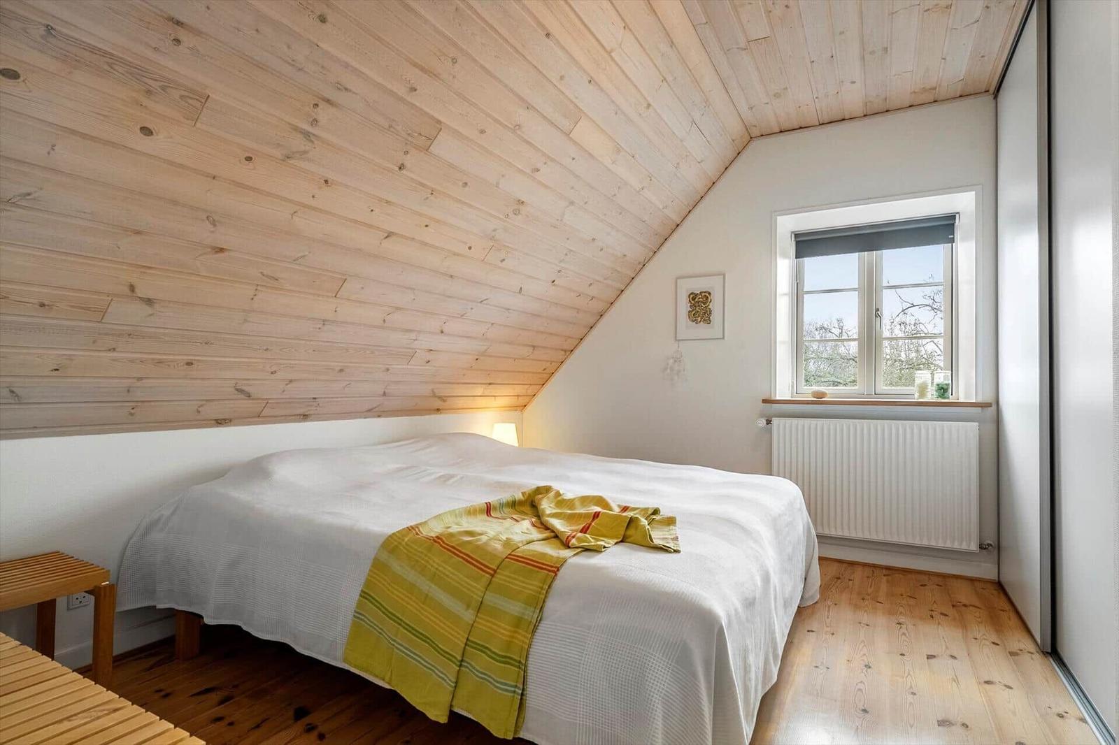 Schlafzimmer mit Holzdach, Bett und Fenster