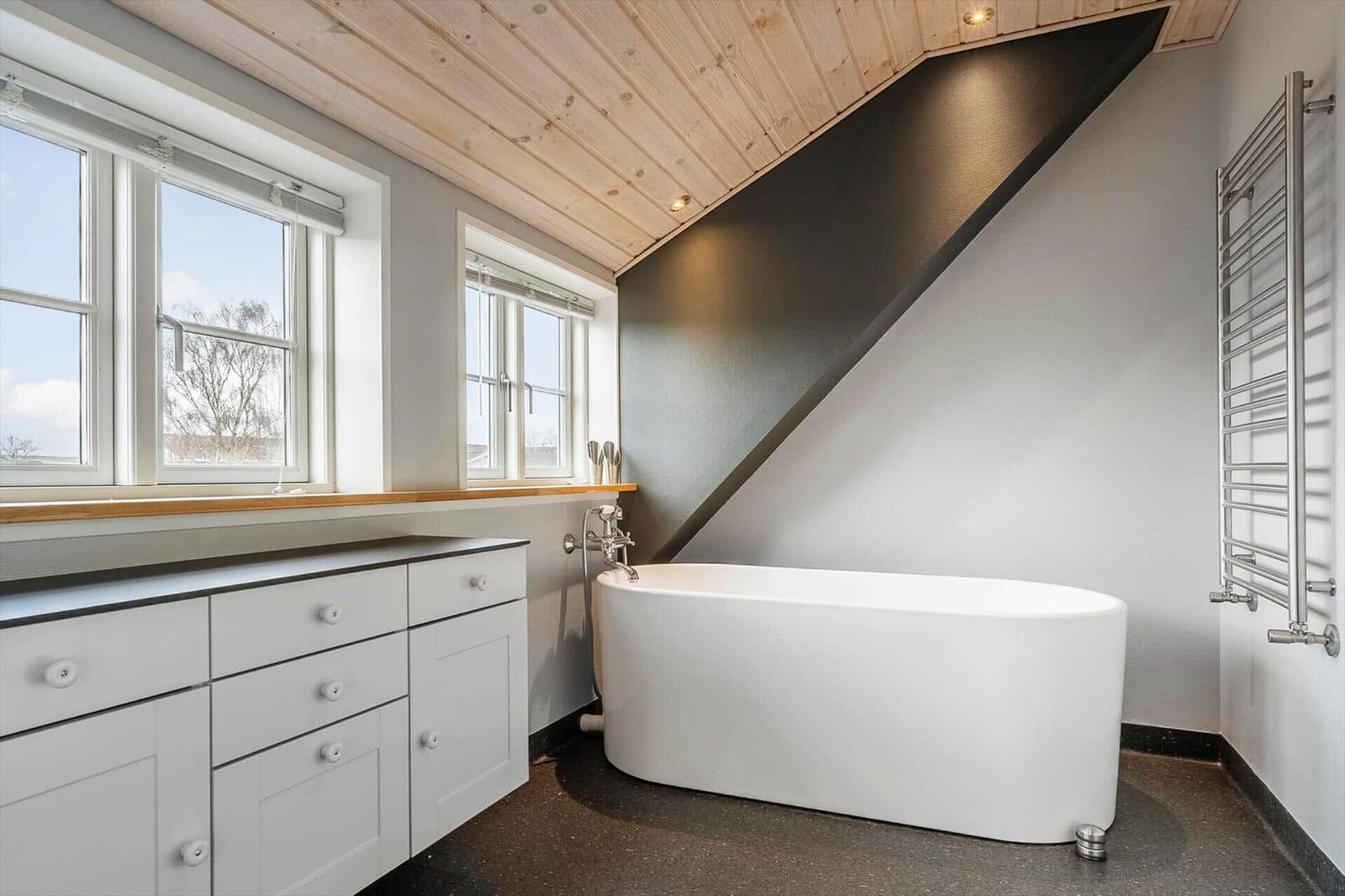 Badezimmer mit freistehender Badewanne, Holzdecke und Fenstern.